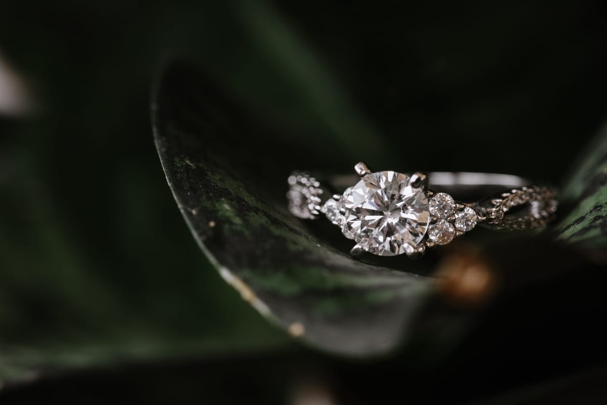 Anillo de compromiso con un diamante central sobre una hoja verde oscura