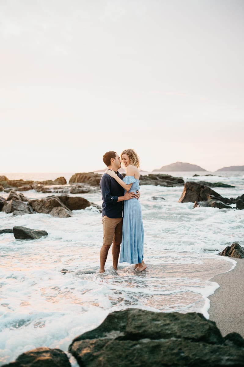 Pareja abrazada en la orilla entre rocas al atardecer
