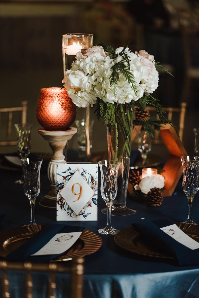 Centro de mesa de boda con hortensias blancas, velas encendidas y el número 9 sobre un mantel azul