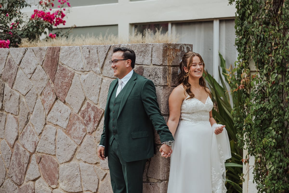 Los novios se toman de la mano frente a un muro de piedra
