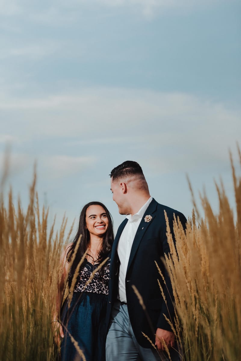 Pareja sonriendo entre pastos altos dorados bajo un cielo azul