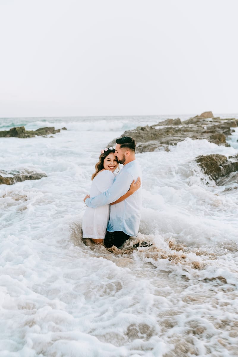 Pareja abrazada entre las olas y las rocas