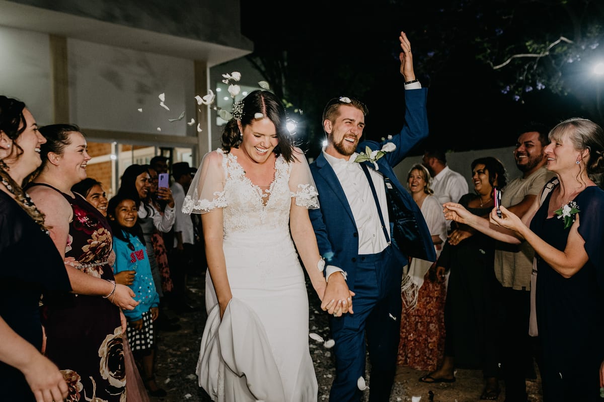 Los novios caminan de la mano entre invitados que lanzan pétalos de noche