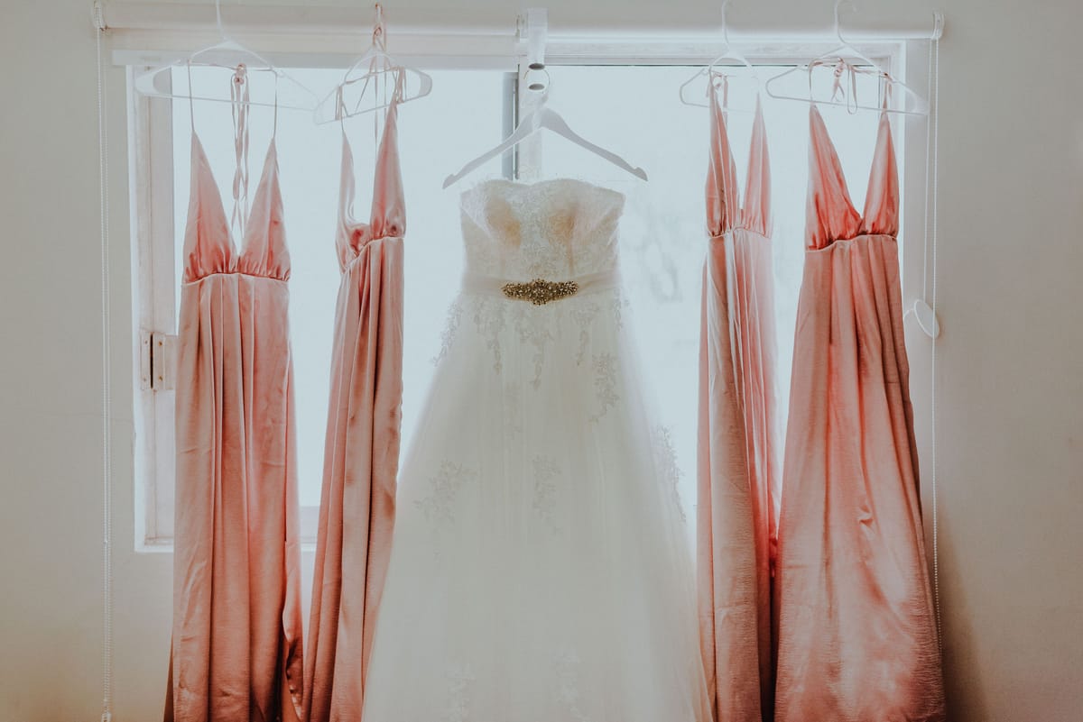 El vestido de novia colgado entre cuatro vestidos rosa frente a una ventana