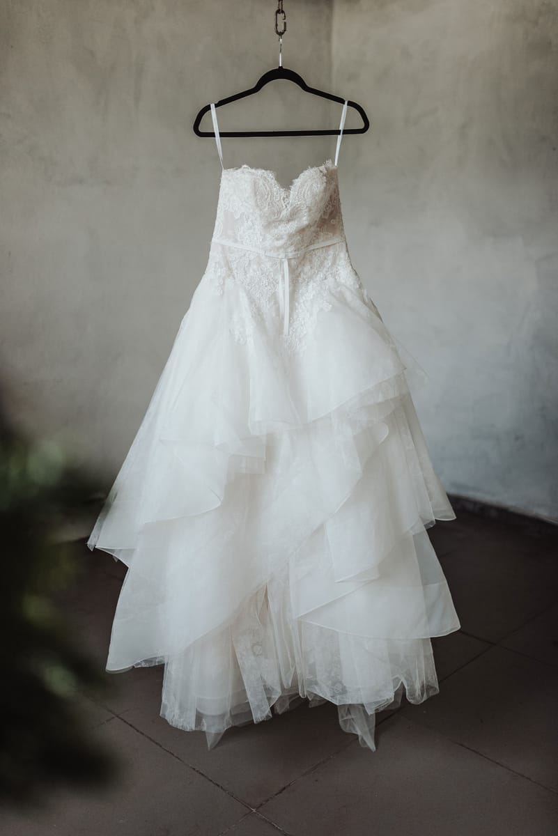 Vestido de novia de encaje y tul colgado de una percha frente a un muro gris