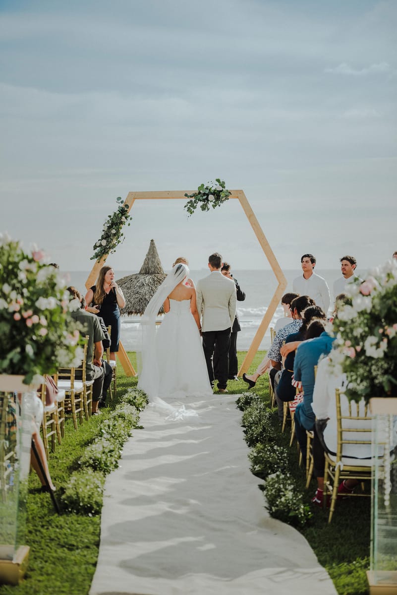 Ceremonia frente al mar con un arco hexagonal y pasillo blanco