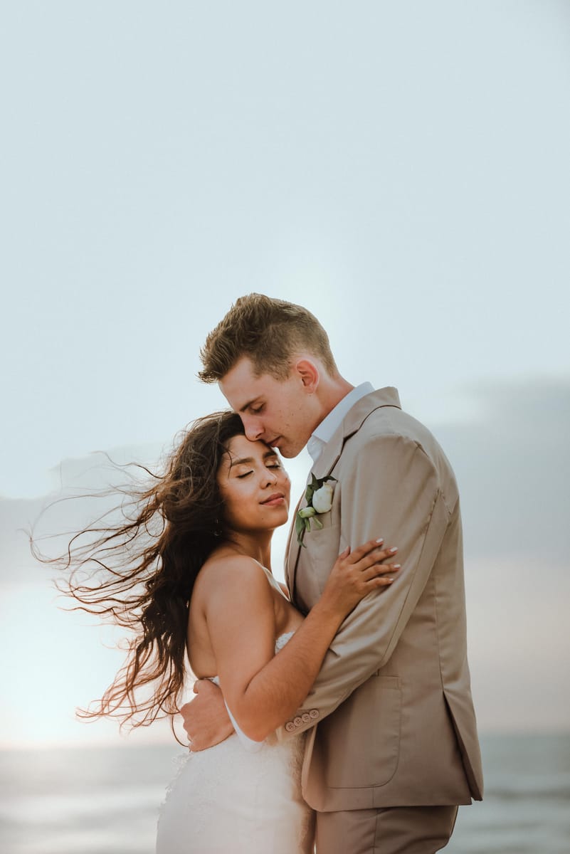 Pareja abrazada junto al mar, el cabello de la novia al viento
