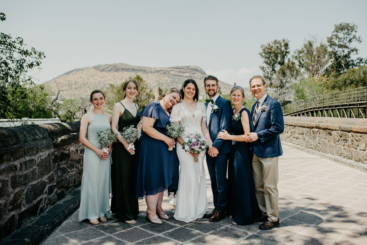 Los novios posan con sus damas y los padres sobre un puente de piedra, con un cerro al fondo